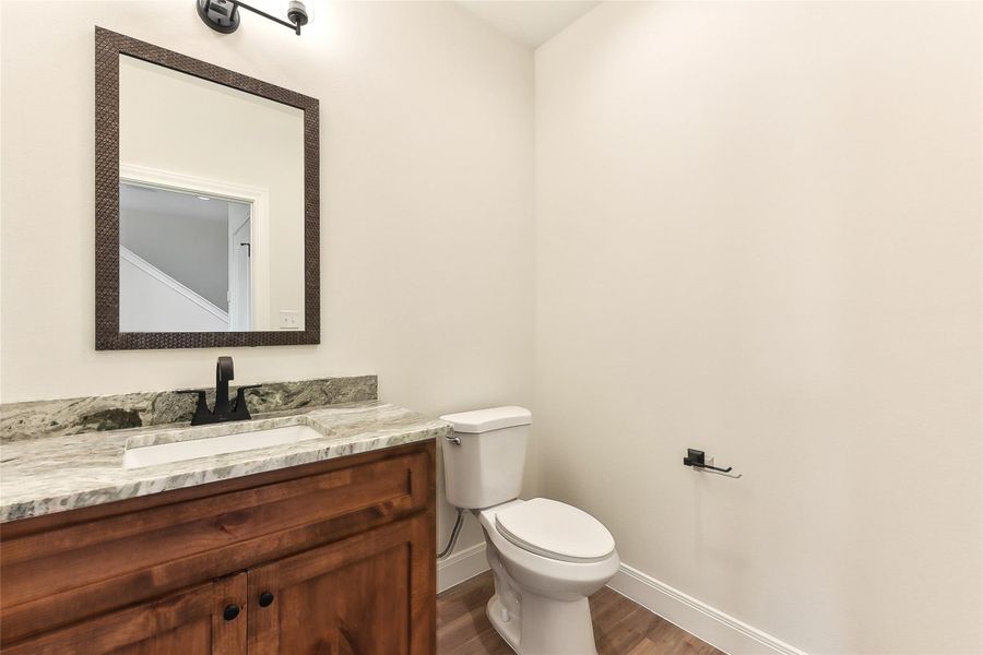 Half bathroom featuring baseboards, toilet, vanity, and wood look floors Half bathroom featuring baseboards, toilet, vanity, and wood look floors