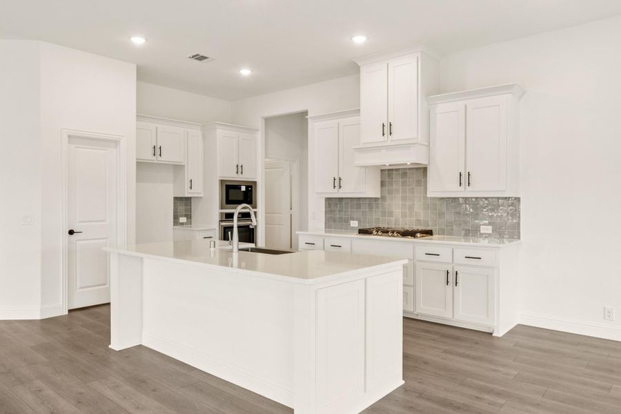 White kitchen with large center island, gray tile backsplash, and dark hardwood floors