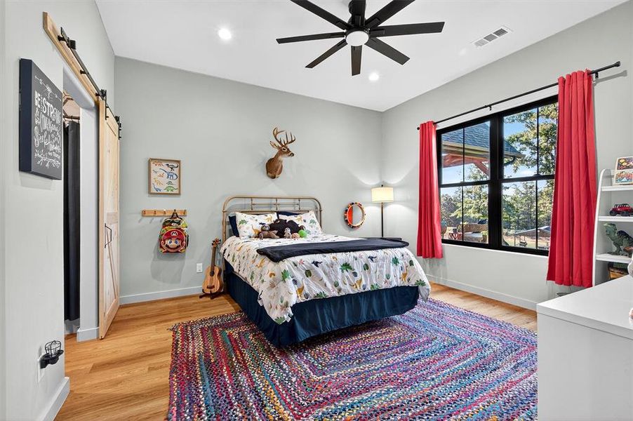 Bedroom with a barn door, light wood-style flooring, recessed lighting, and ceiling fan Bedroom with a barn door, light wood-style flooring, recessed lighting, and ceiling fan