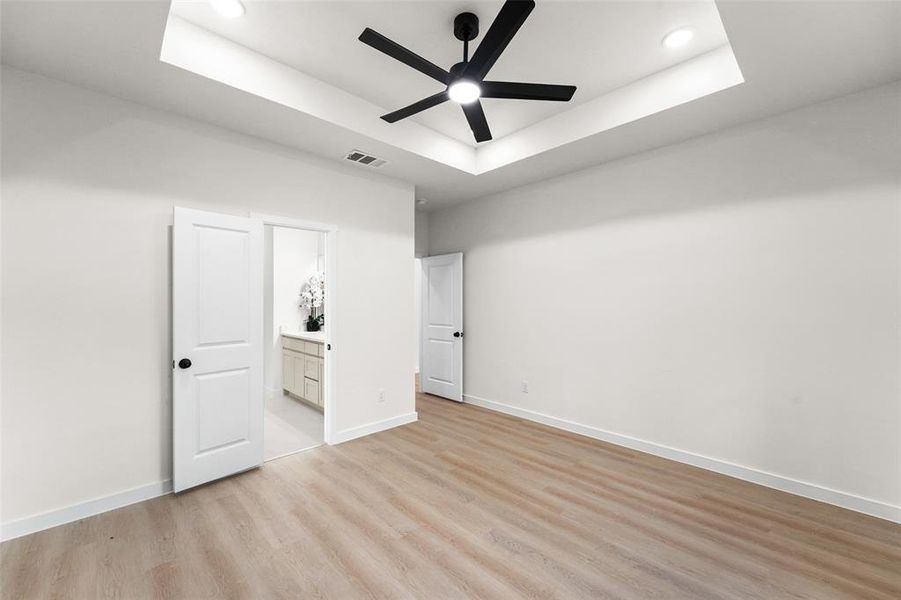 Spacious interior room featuring wood-finish flooring, a tray ceiling with recessed lighting, and a contemporary ceiling fan Spacious interior room featuring wood-finish flooring, a tray ceiling with recessed lighting, and a contemporary ceiling fan