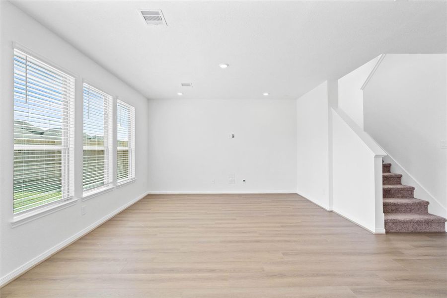 This bright and airy Great Room offers a spacious layout ideal for both relaxing evenings and lively gatherings. Designed for comfort and connection, it features Heartland Ranch Homespun Brown vinyl plank flooring, large windows with blinds, high ceilings, recessed lighting, and seamless access to the stunning kitchen and dining—perfect for everyday living and entertaining alike.