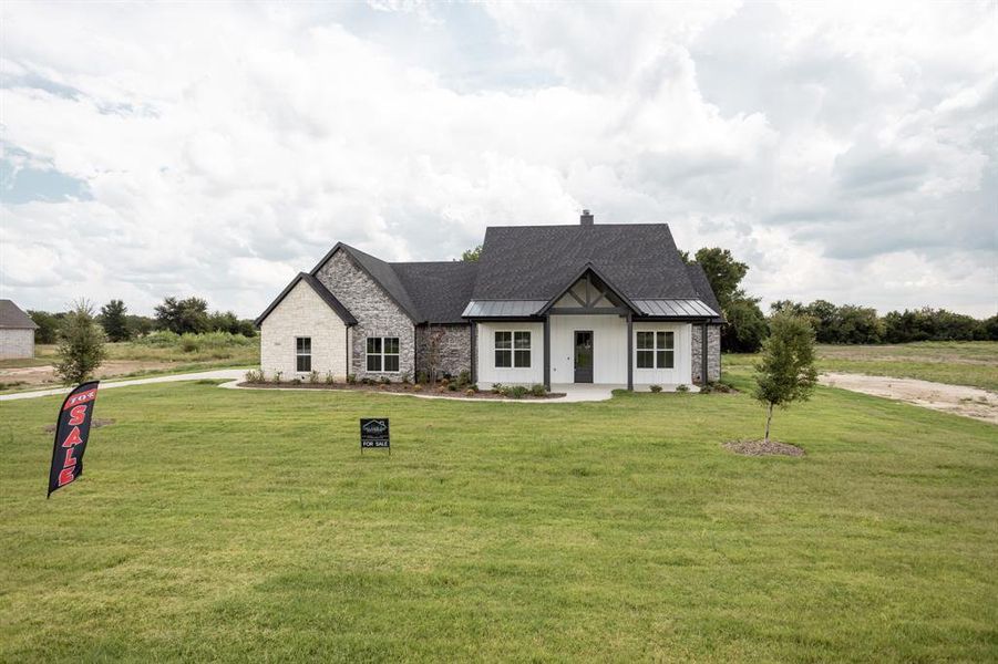 View of front facade featuring a standing seam roof, stone siding, a front lawn, and a metal roof View of front facade featuring a standing seam roof, stone siding, a front lawn, and a metal roof