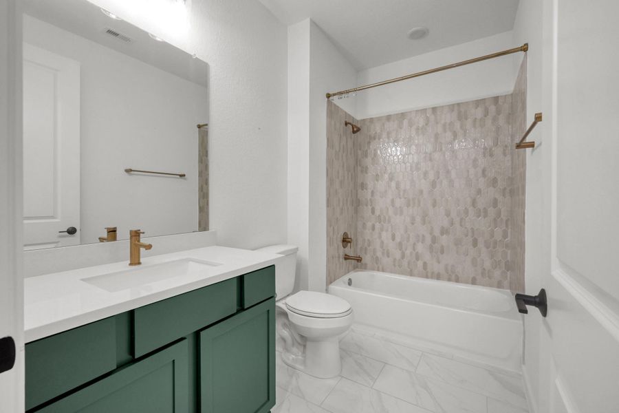 The secondary bathroom has tile flooring and a tub/shower combo. There are gold toned faucets in the sink and tub. Love the green cabinet with the gold tones.
