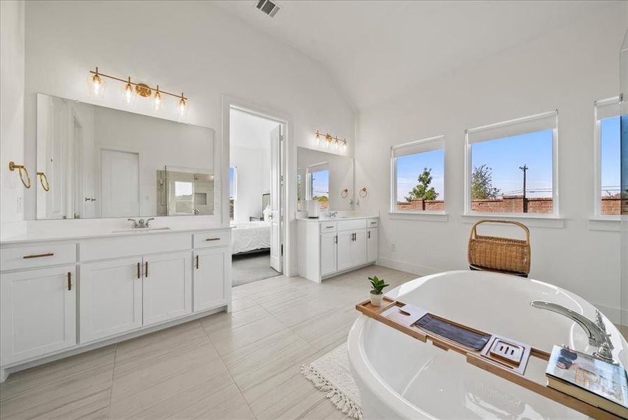 Bathroom with visible vents, lofted ceiling, a soaking tub, a sink, and two vanities