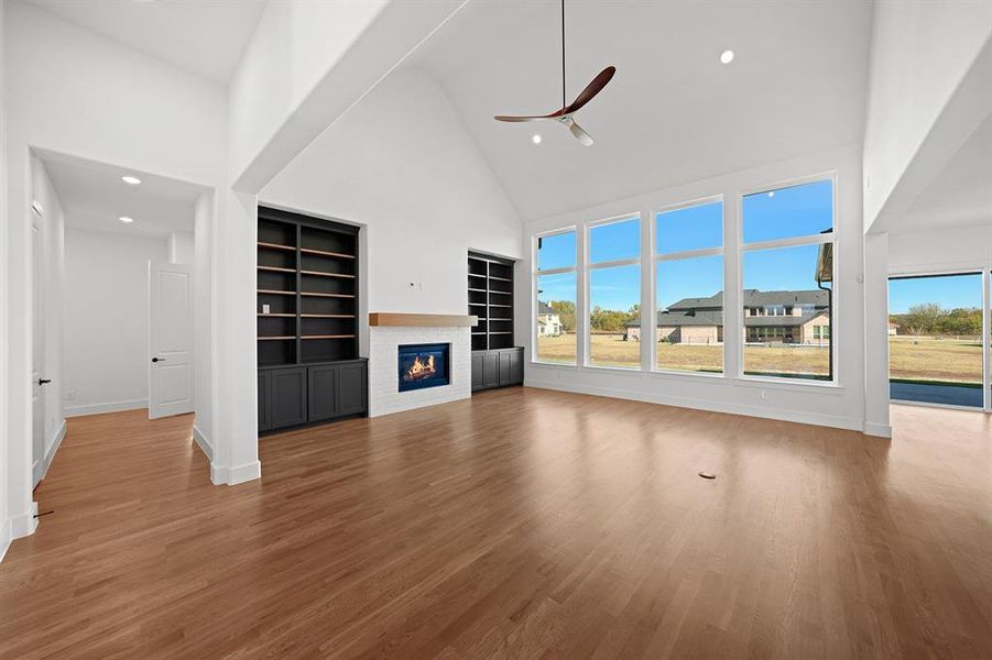 Unfurnished living room with high vaulted ceiling, a glass covered fireplace, light wood-style floors, recessed lighting, and a ceiling fan