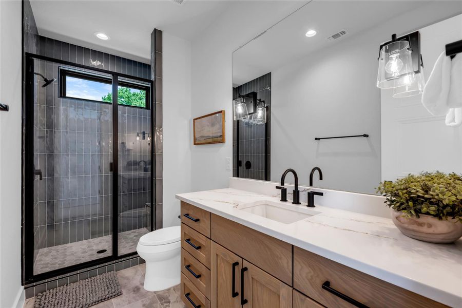 Bathroom two: featuring a wood-finish vanity with a light-toned countertop, a shower enclosure with black framing and vertical grey tile, and matte black fixtures