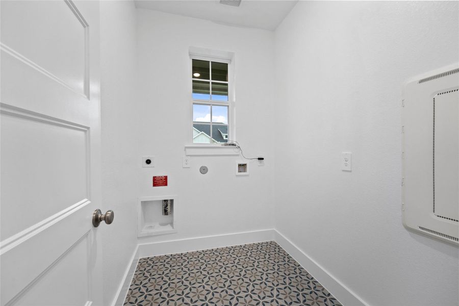 This bright and functional laundry room is conveniently located and ready for your appliances. It features clean white walls and trim, window providing abundant natural light, and an eye-catching patterned floor tile that adds a touch of personality.