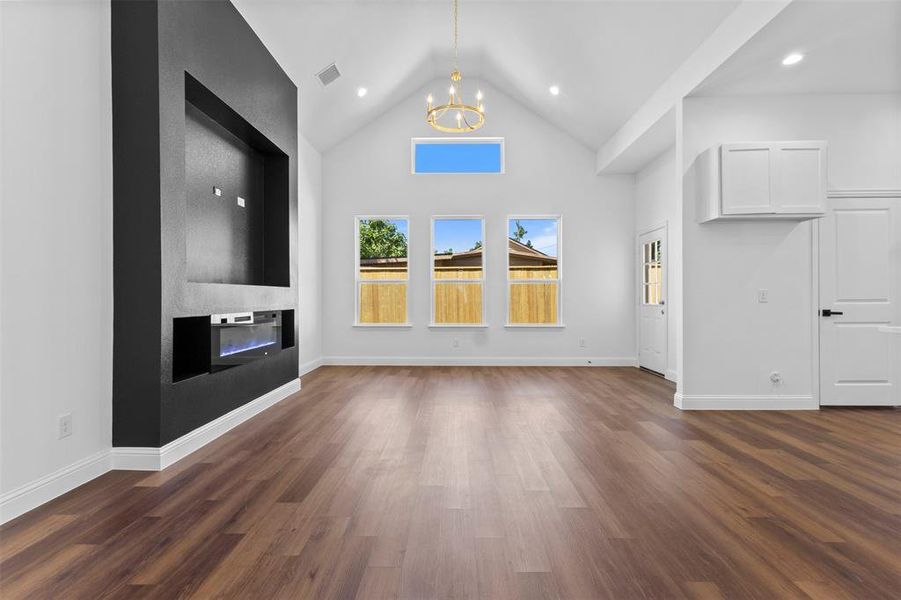 Unfurnished living room featuring a chandelier, dark wood-type flooring, high vaulted ceiling, a large fireplace, and recessed lighting Unfurnished living room featuring a chandelier, dark wood-type flooring, high vaulted ceiling, a large fireplace, and recessed lighting