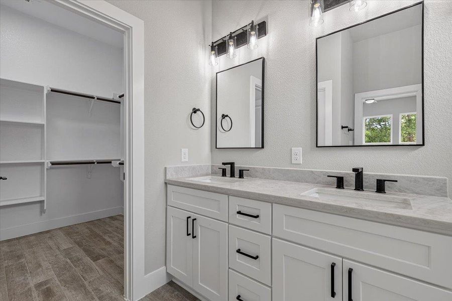 A well-appointed primary bathroom featuring a double vanity with ample counter space and an adjacent walk-in closet. A well-appointed primary bathroom featuring a double vanity with ample counter space and an adjacent walk-in closet.