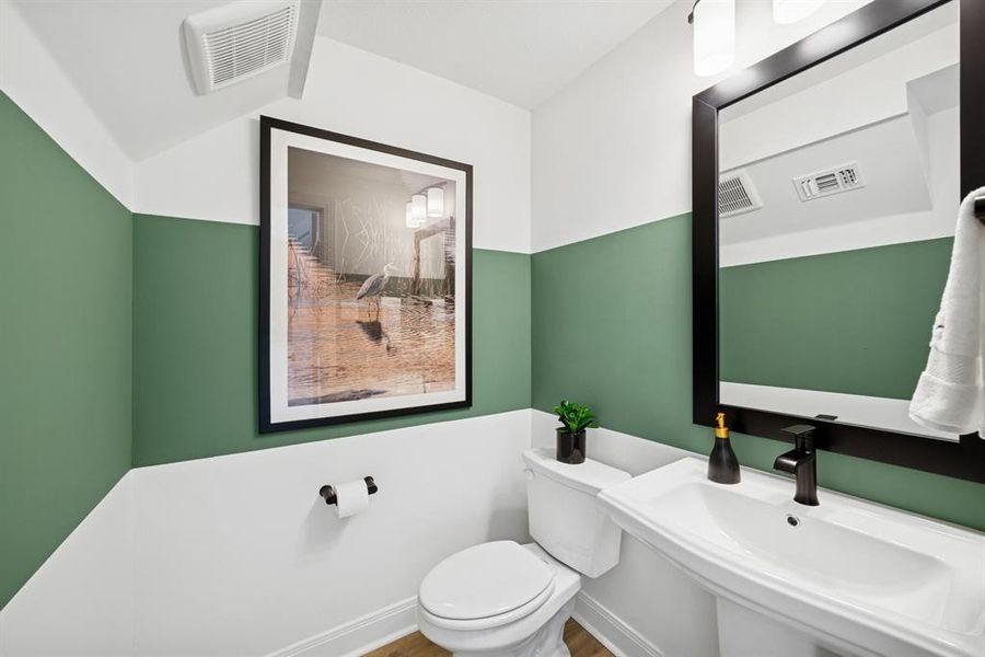 Pedestal sink with matte black faucet, wall-mounted mirror with black frame, and two-tone wall treatment