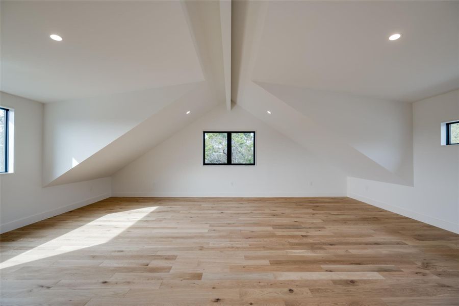 Bonus room with light wood-type flooring and vaulted ceiling with beams