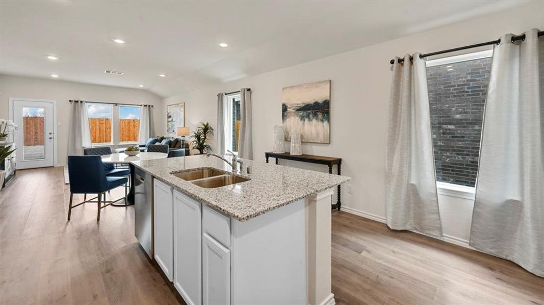 Kitchen with white cabinetry, light stone countertops, open floor plan, a kitchen island with sink, and light wood-style floors Kitchen with white cabinetry, light stone countertops, open floor plan, a kitchen island with sink, and light wood-style floors