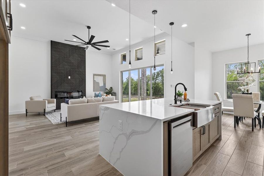 Kitchen with light stone counters, an island with sink, light wood finished floors, crown molding, and dishwasher