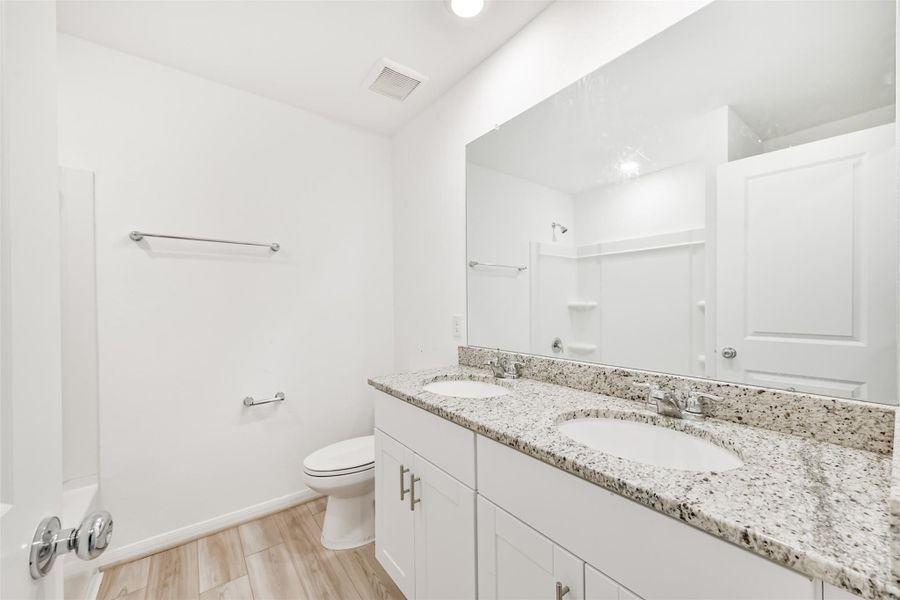 This secondary bathroom features double sinks with granite countertops, modern fixtures, and a spacious shower.