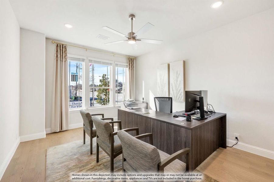 Home office with dark wood desk, ceiling fan, hardwood floors, and two guest chairs near bright windows