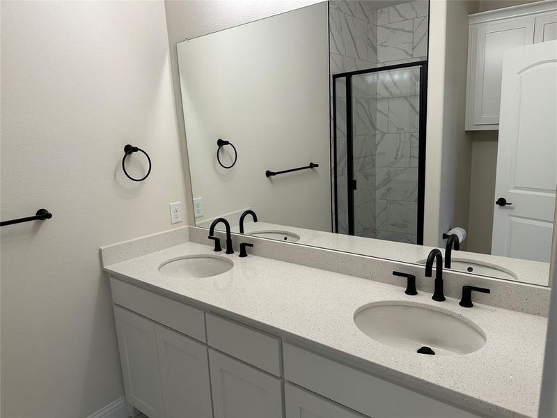 Bathroom featuring a stall shower, a sink, and double vanity