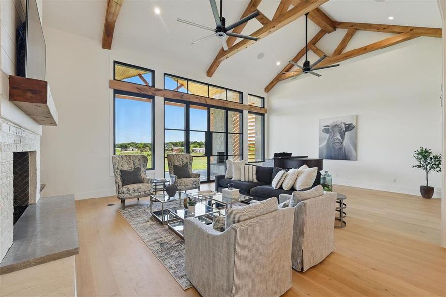 Living area featuring a ceiling fan, high vaulted ceiling, beamed ceiling, light wood-style floors, and a brick fireplace Living area featuring a ceiling fan, high vaulted ceiling, beamed ceiling, light wood-style floors, and a brick fireplace