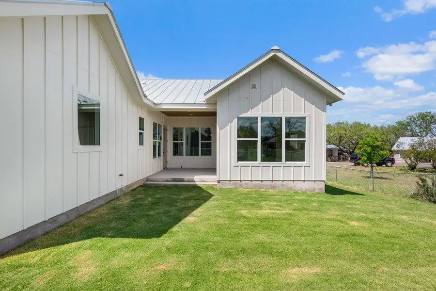 The property features a white exterior with board and batten siding, a metal roof, and an expansive green lawn