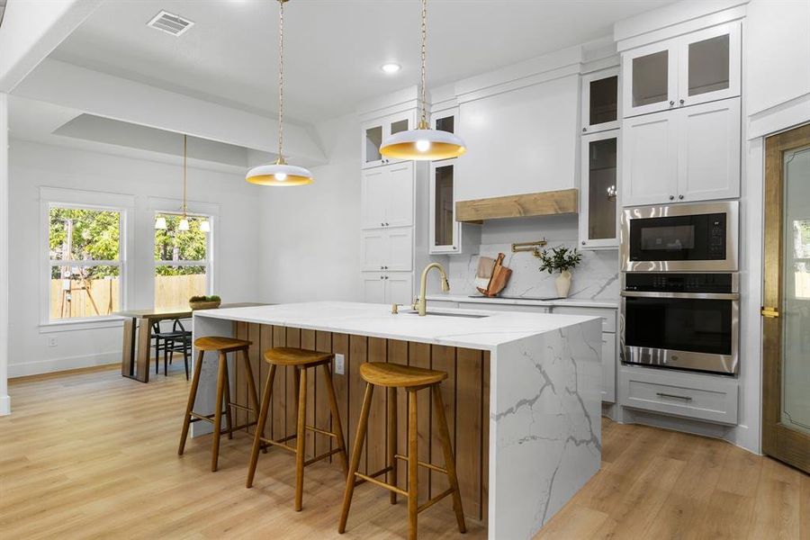 Kitchen featuring white cabinets, an island with sink, stainless steel appliances, sink, and decorative light fixtures