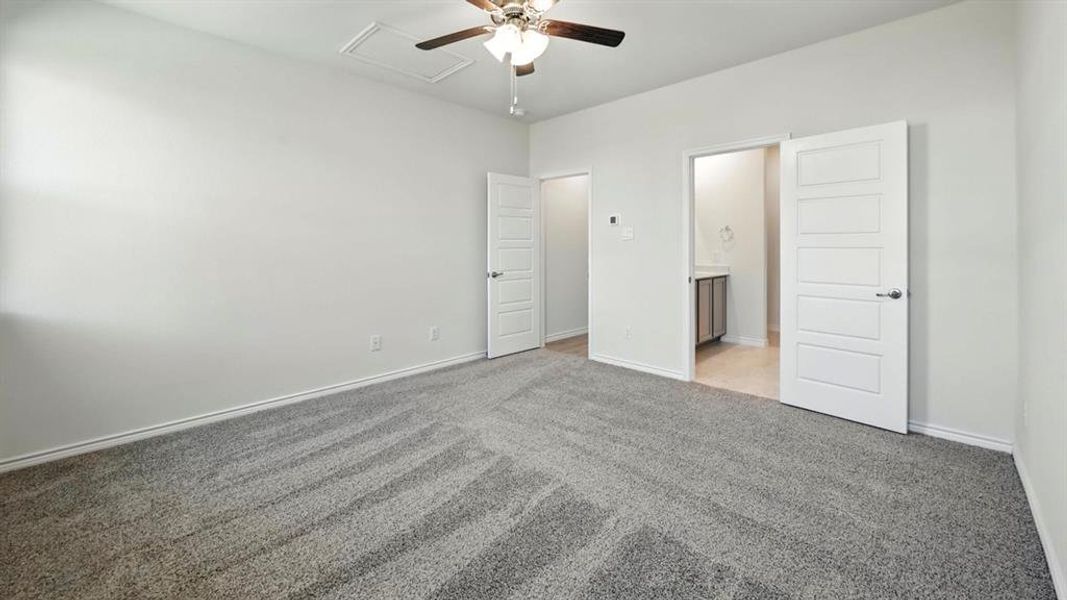 Unfurnished bedroom with attic access, connected bathroom, light colored carpet, and ceiling fan