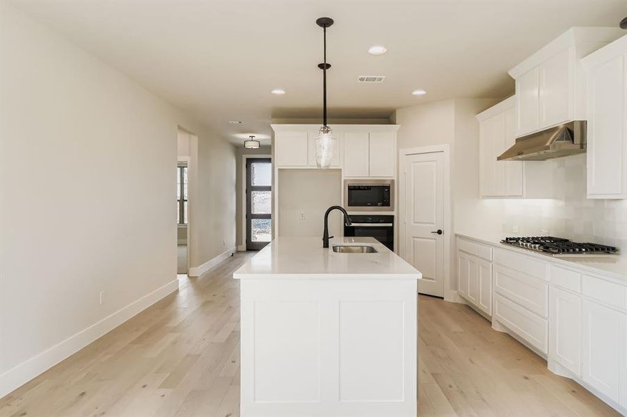Kitchen with light wood finished floors, appliances with stainless steel finishes, recessed lighting, and white cabinetry