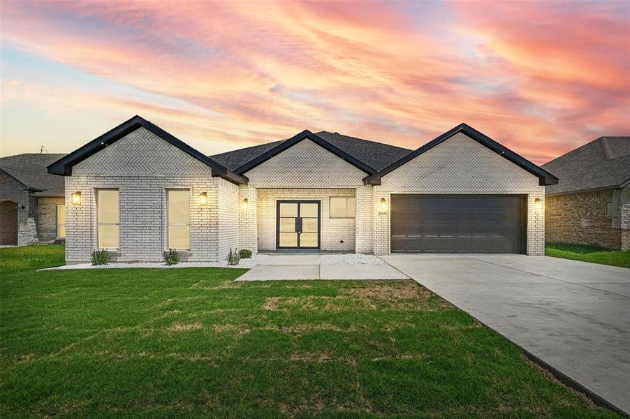 View of front of house featuring driveway, a yard, an attached garage, and brick siding