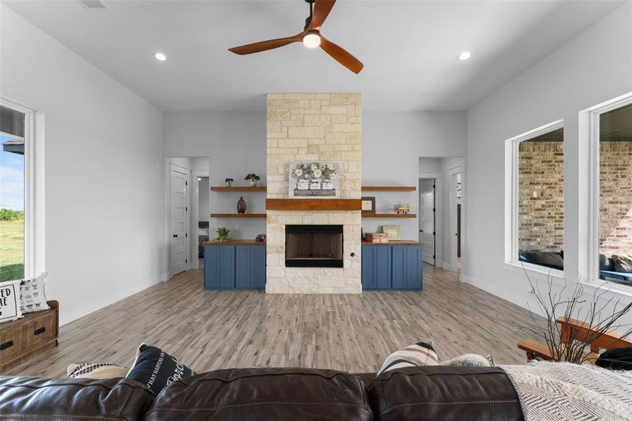 Living area featuring a stone fireplace with a wood mantle, built-in shelving, blue cabinetry, wood-finish flooring, and recessed lighting