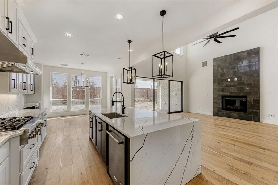 Kitchen with dual tone cabinets, light stone countertops, a tiled fireplace, light wood finished floors, and suspended lighting