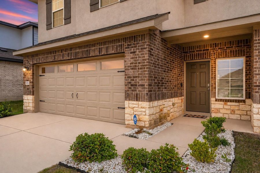 Exterior featuring a two-car garage, brick facade with stone accents, a covered entry, and a well-maintained concrete driveway Exterior featuring a two-car garage, brick facade with stone accents, a covered entry, and a well-maintained concrete driveway