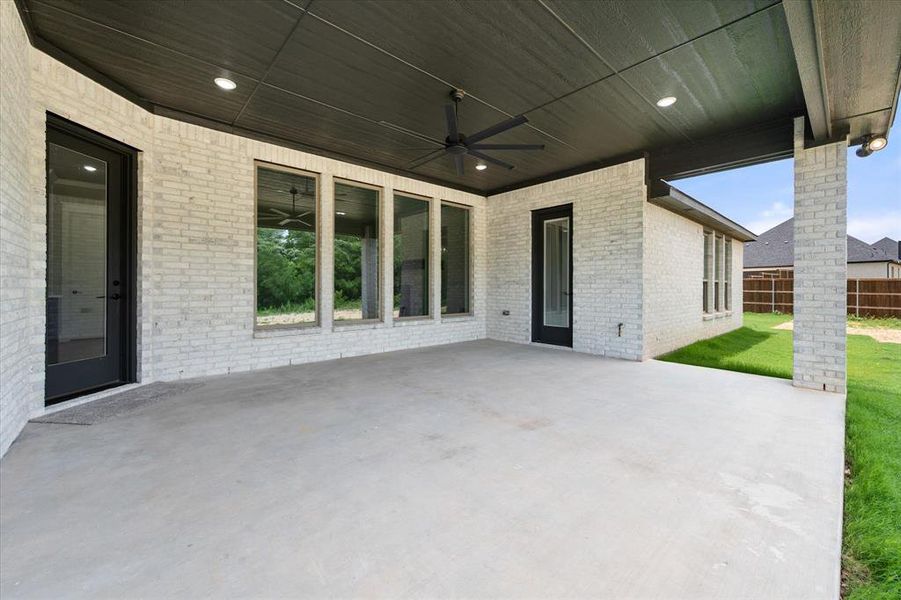 Expansive covered patio featuring a concrete surface, white brick exterior, black ceiling with recessed lighting, and a ceiling fan