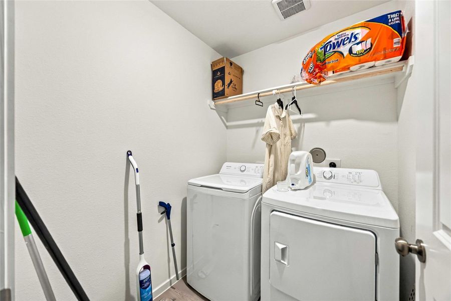 Convenient laundry room featuring a washer and dryer set, ample shelving for storage, and space for cleaning supplies.