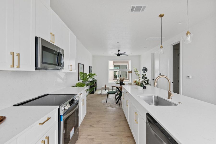 Modern kitchen featuring white cabinetry, stainless steel appliances, a large island with an undermount sink, pendant lighting, and wood-finish flooring