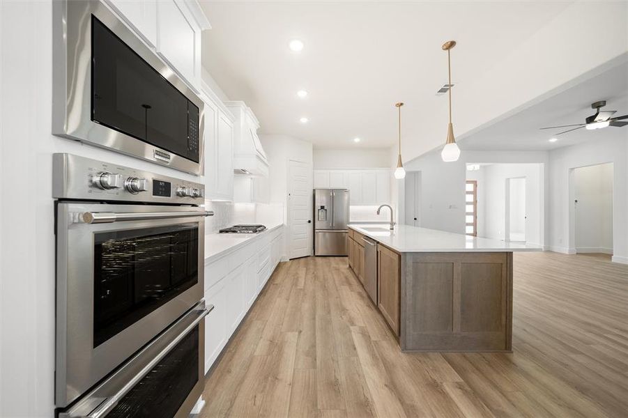 Kitchen featuring appliances with stainless steel finishes, light wood-style floors, light countertops, a center island with sink, and recessed lighting