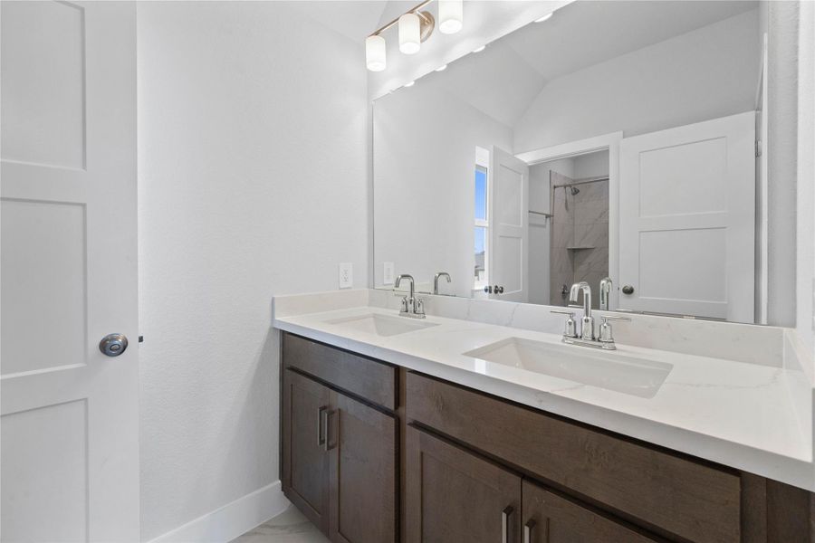 This well-appointed secondary bathroom offers exceptional functionality with its rich, dark wood double vanity topped with pristine white countertops and convenient dual undermount sinks. Sleek, polished chrome fixtures complement the expansive vanity mirror and chic light vanity fixture.