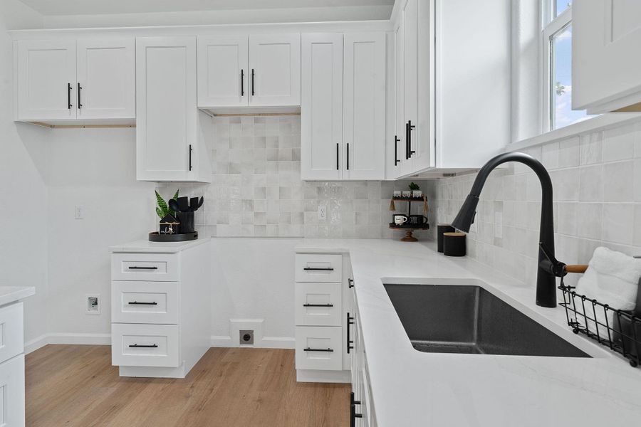 Kitchen with light wood-style floors, tasteful backsplash, and white cabinetry