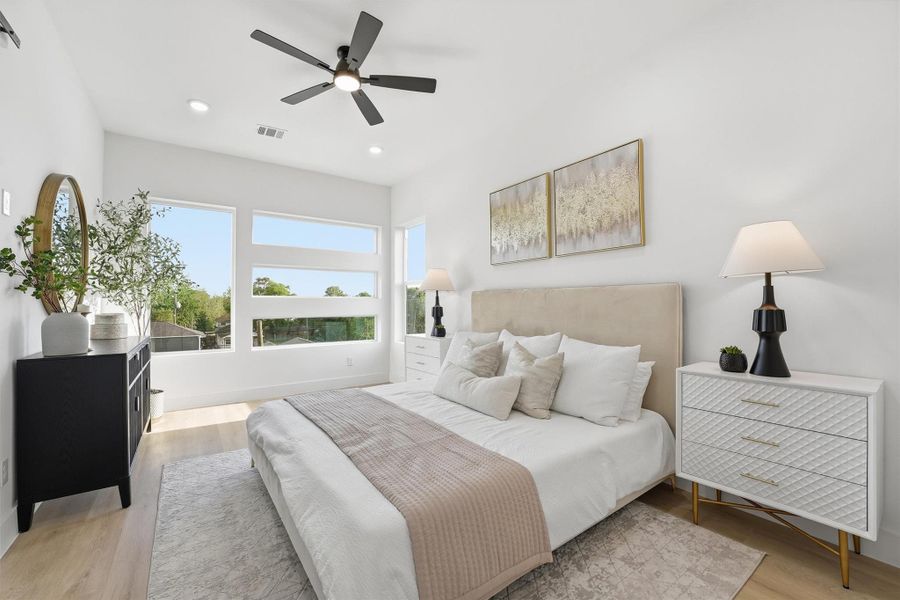 Spacious and serene primary bedroom featuring wood-look flooring, recessed lighting, a modern ceiling fan, and oversized windows that fill the room with natural light, creating a bright and relaxing retreat.