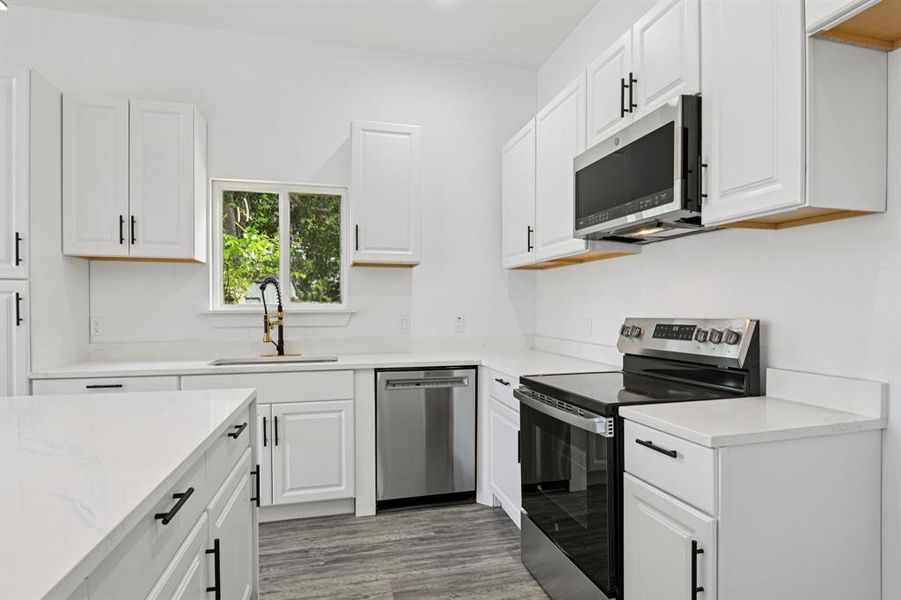 Kitchen featuring stainless steel appliances, white cabinetry, light wood-style flooring, light stone counters, and recessed lighting Kitchen featuring stainless steel appliances, white cabinetry, light wood-style flooring, light stone counters, and recessed lighting