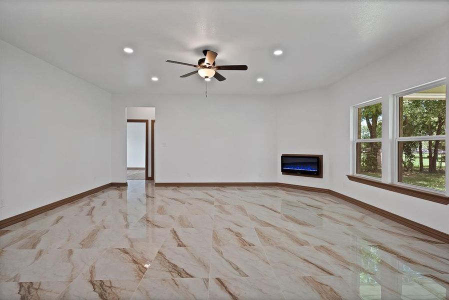 Unfurnished living room with recessed lighting, ceiling fan, light marble finish floors, and a glass covered fireplace