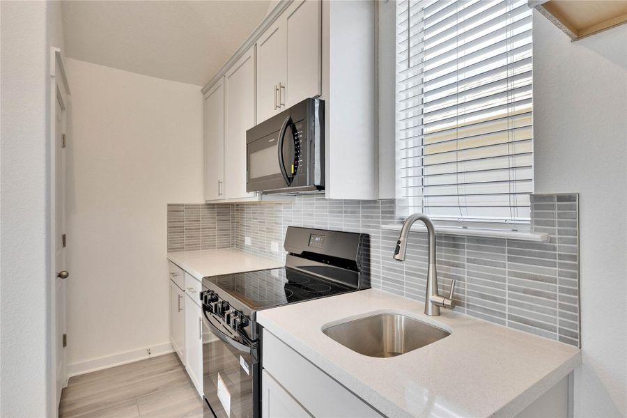 Kitchen with black appliances, tasteful backsplash, light stone counters, and white cabinetry