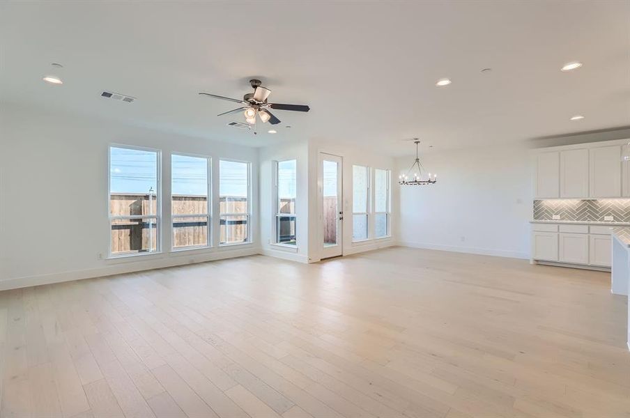 Unfurnished living room with a wealth of natural light, ceiling fan with notable chandelier, and light wood-type flooring