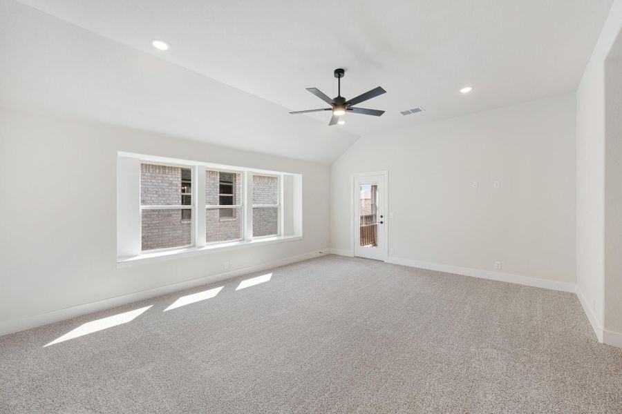 Empty room with vaulted ceiling, ceiling fan, carpet flooring, large windows, and a glass back door