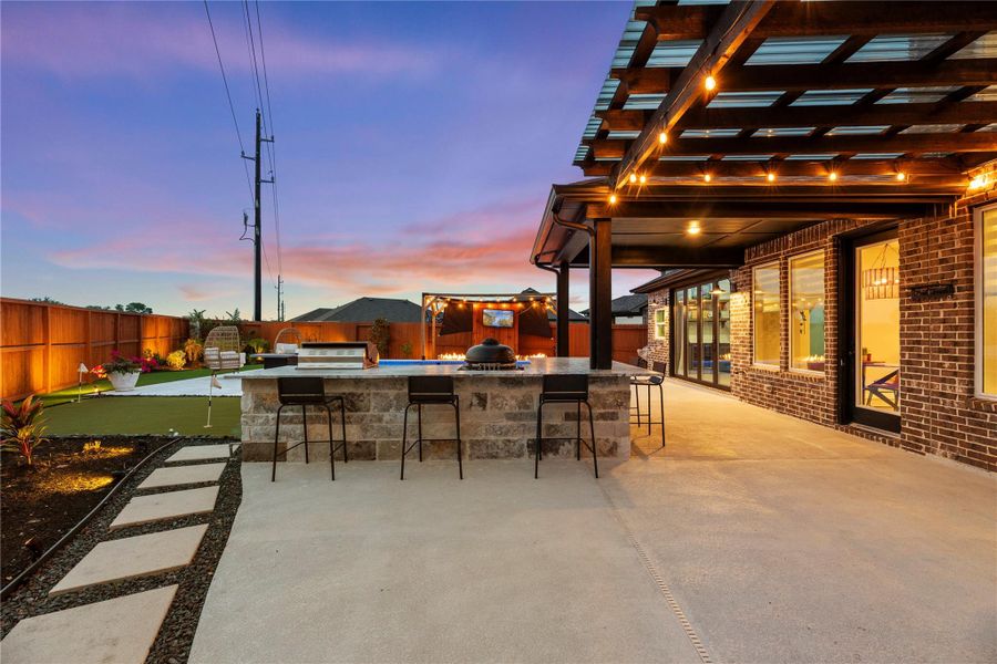 The outdoor kitchen has bar seating and the yard is well-lit with up accent lighting.