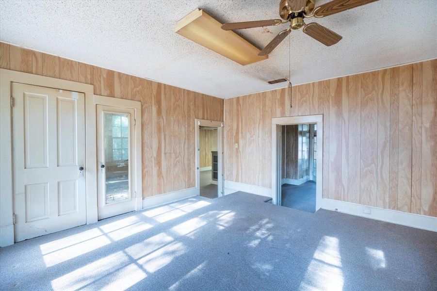 Carpeted spare room featuring ceiling fan, wood walls, and a textured ceiling