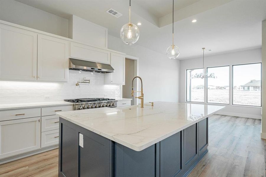 Example of builders Kitchen w white cabinets, decorative light fixtures, light stone countertops