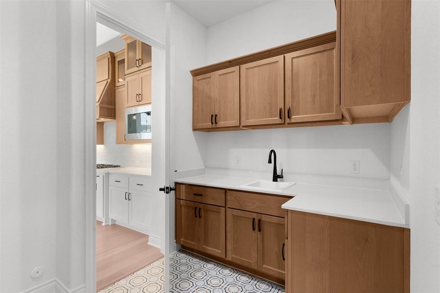This utility area features white countertops, a sink with a matte black faucet, and natural wood cabinetry
