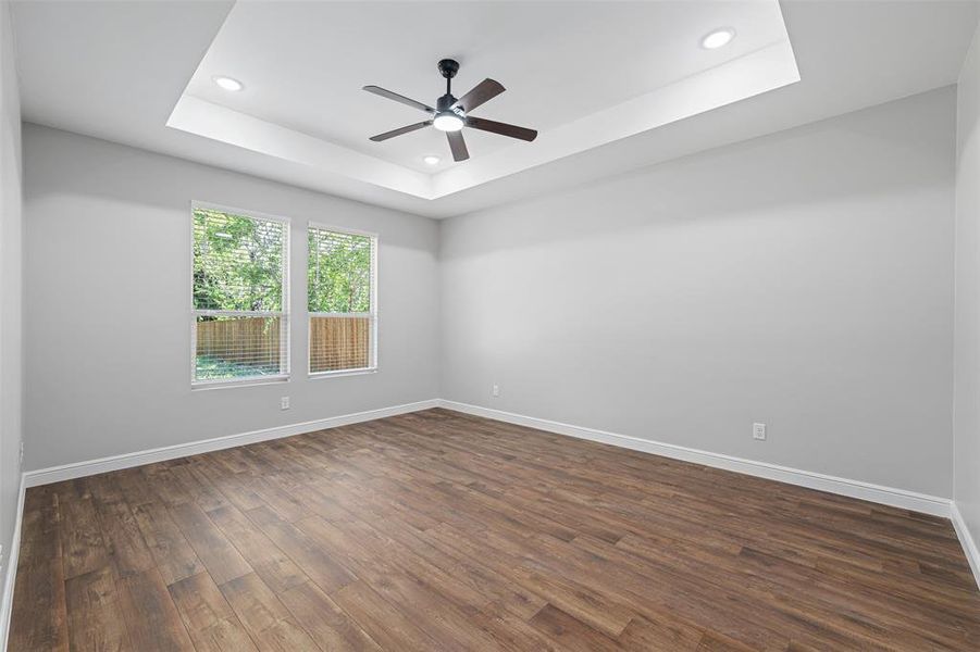 Empty room featuring ceiling fan, dark wood-type flooring, and a raised ceiling