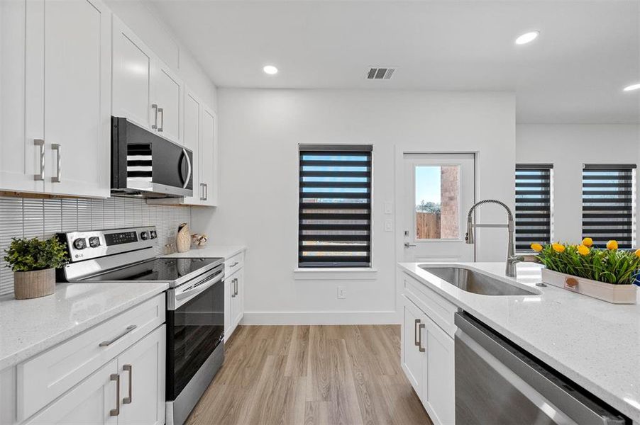 Kitchen with visible vents, white cabinets, light stone counters, appliances with stainless steel finishes, and a sink