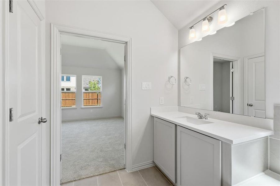 Bathroom with vanity, light colored carpet, light tile patterned floors, and lofted ceiling