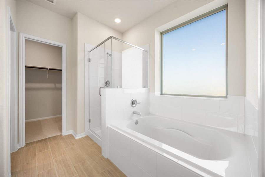 A deep, built-in soaking tub sits beneath a large rain glass window, creating an ideal spot for unwinding. The primary bathroom also features a sleek, frameless glass walk-in shower with white tile surround and modern chrome fixtures. A deep, built-in soaking tub sits beneath a large rain glass window, creating an ideal spot for unwinding. The primary bathroom also features a sleek, frameless glass walk-in shower with white tile surround and modern chrome fixtures.