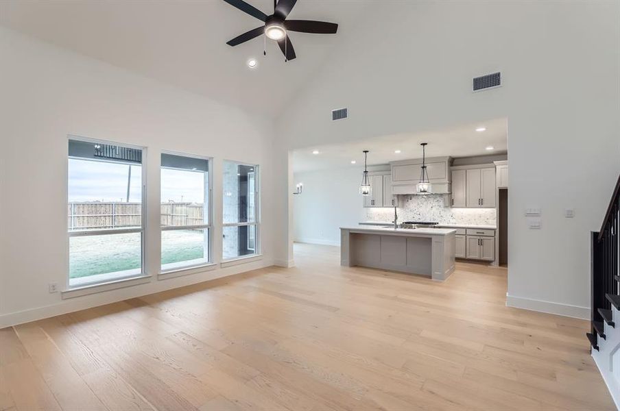 Kitchen with light hardwood / wood-style flooring, high vaulted ceiling, pendant lighting, gray cabinets, and a center island with sink